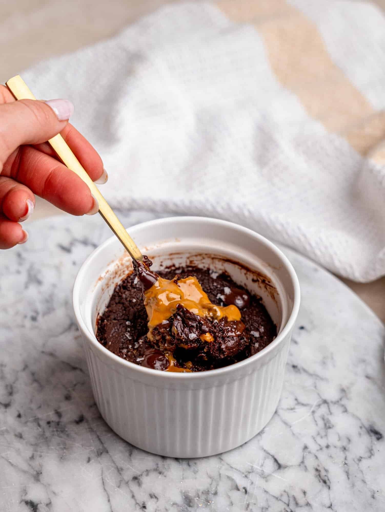 1. Chocolate protein mug cake filled with Biscoff spread and melted chocolate, served with a spoon in a white ramekin.