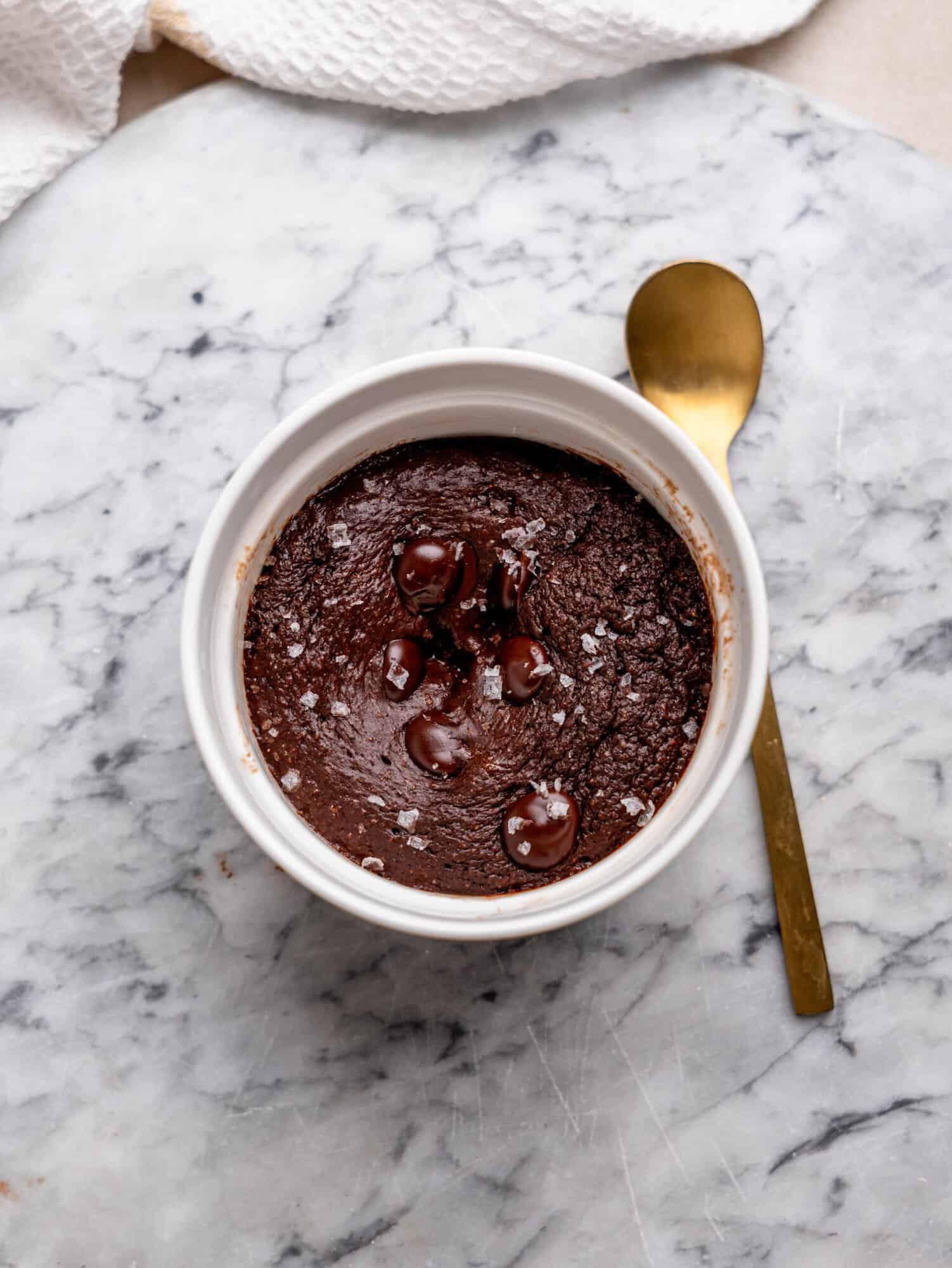 Chocolate protein mug cake topped with chocolate chips and flaky sea salt, served in a white ramekin.