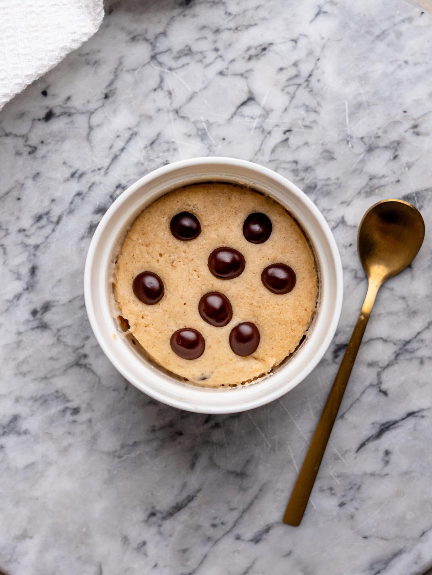 Baked chocolate chip protein mug cake in a white ramekin, viewed from above and topped with chocolate chips.