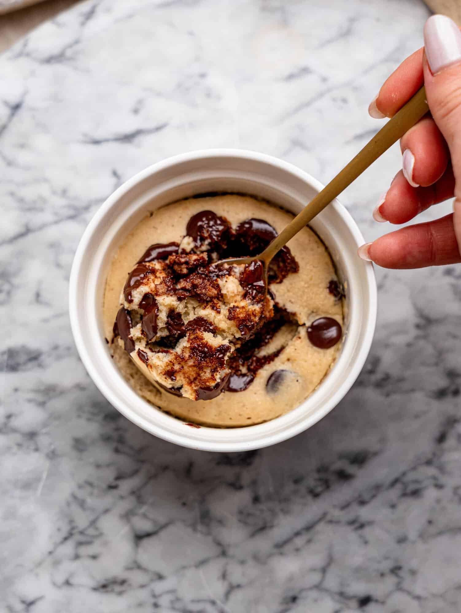 Chocolate chip protein mug cake with a spoonful of the cake lifted from the center, revealing melted chocolate chips and a soft interior.