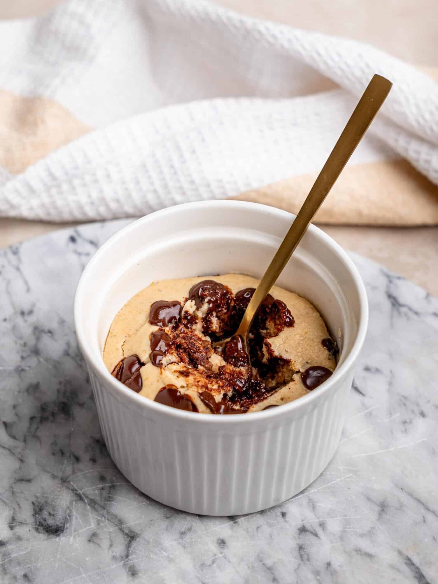 1. Chocolate chip protein mug cake in a white ramekin with melted chocolate chips and a spoon inserted into the cake.