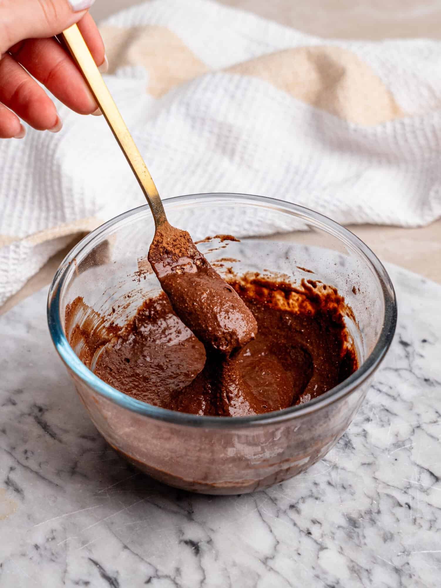 Chocolate protein mug cake batter being stirred in a glass bowl with a gold fork.
