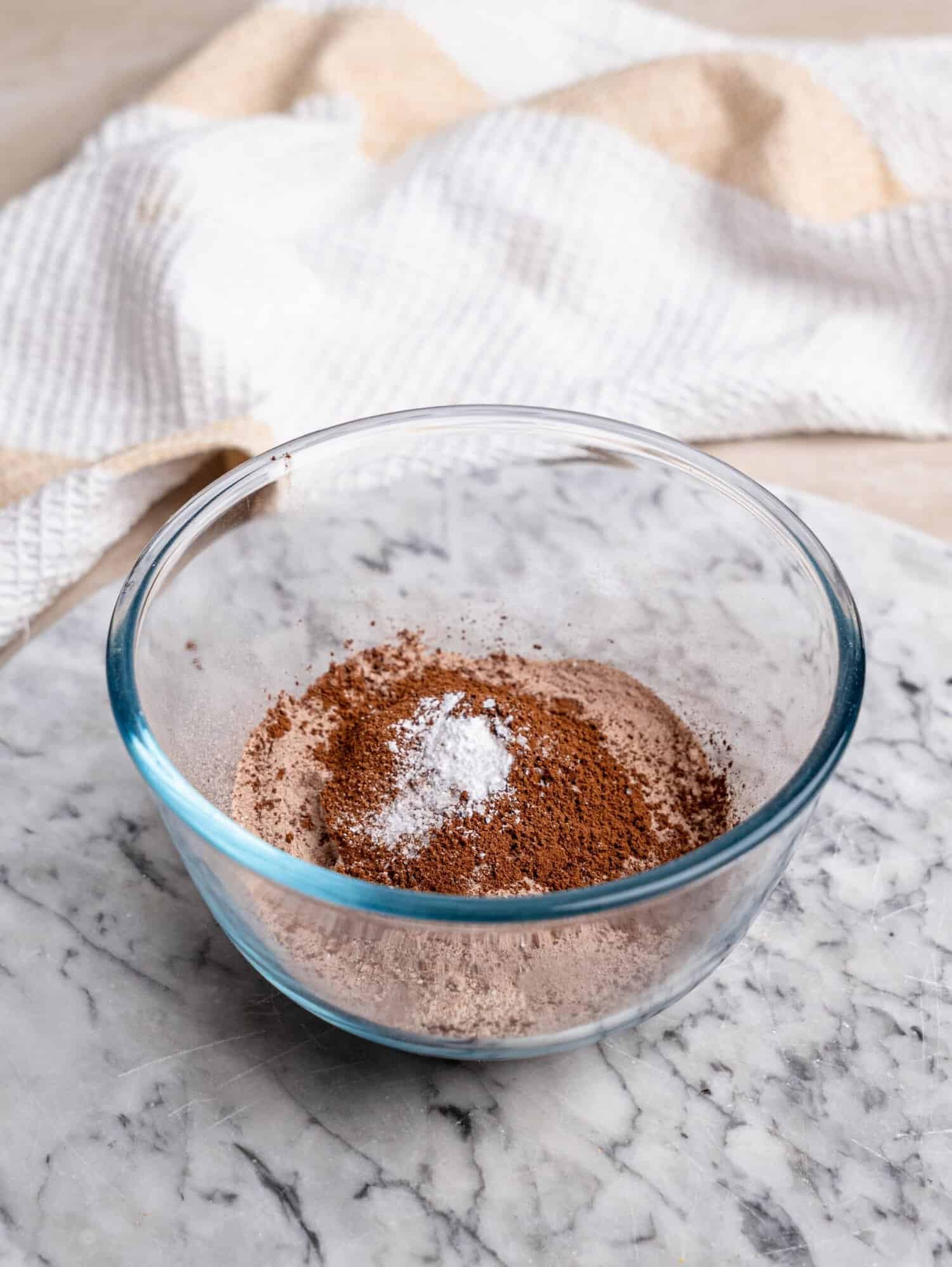 1. Dry ingredients for a chocolate protein mug cake, including protein powder, cocoa powder, and baking powder, in a glass bowl.