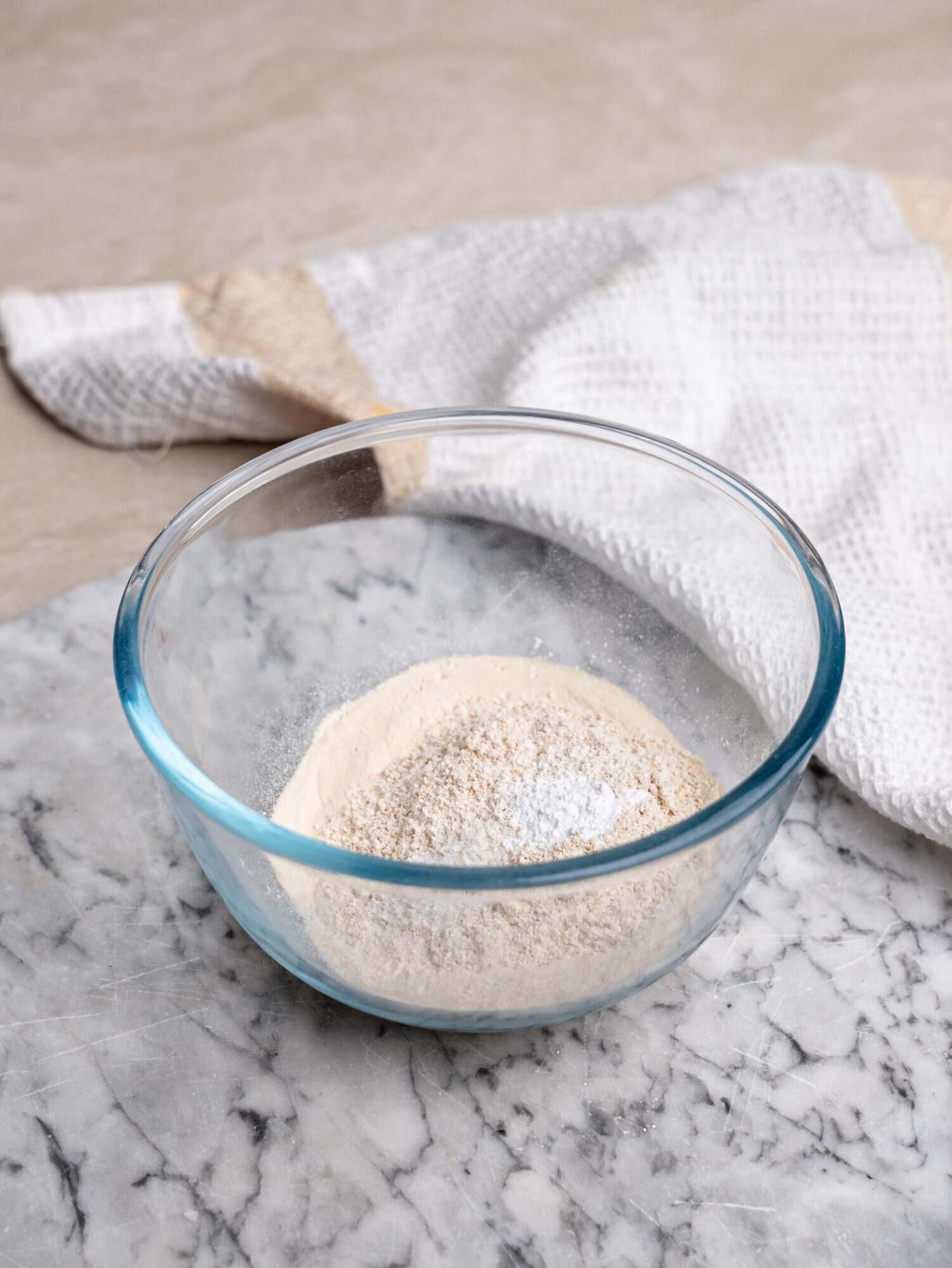 Protein mug cake dry ingredients, including oat flour, protein powder, and baking powder, mixed in a glass bowl.
