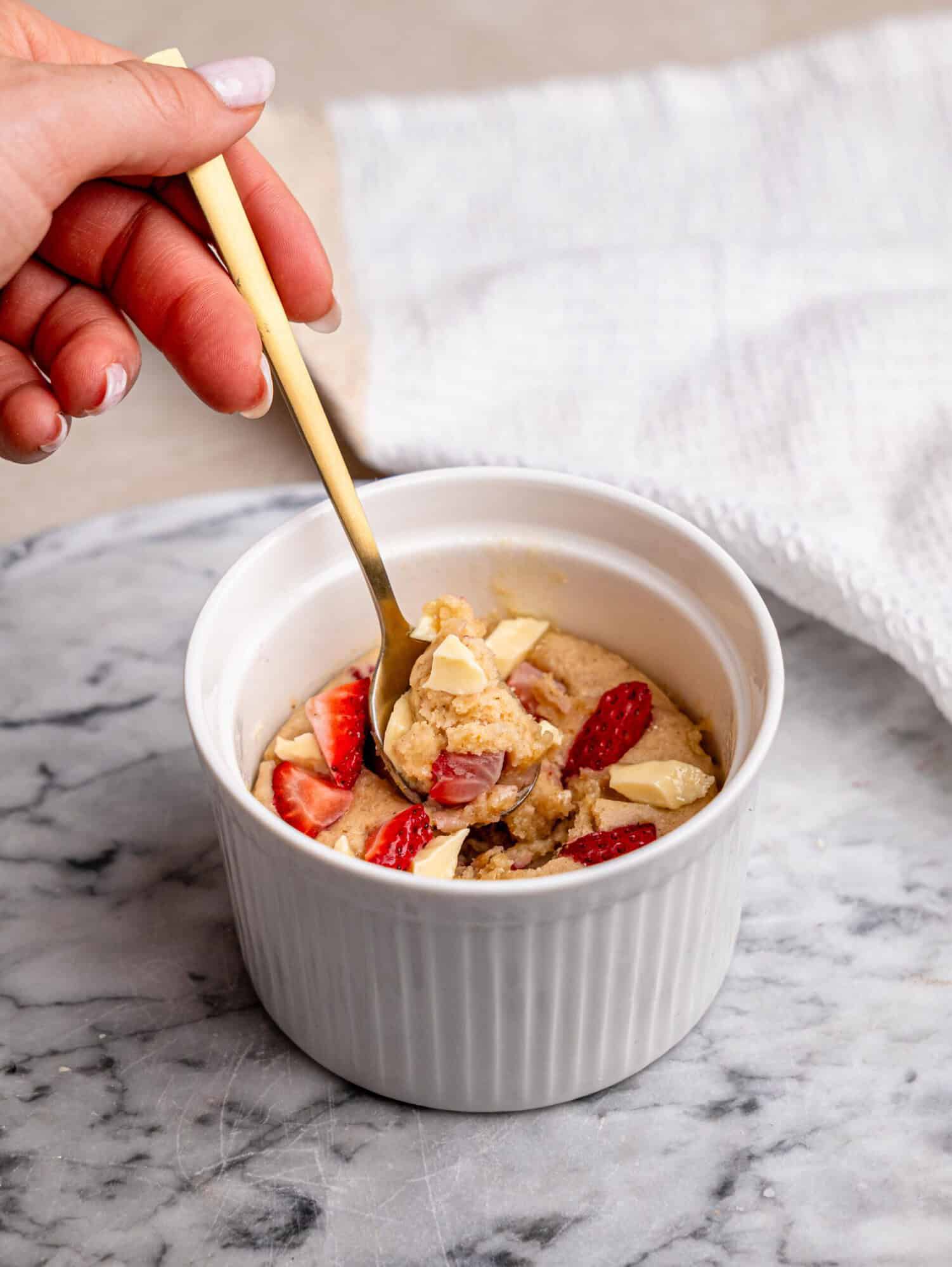 Strawberry white chocolate protein mug cake topped with fresh strawberries and white chocolate pieces, served in a white ramekin.