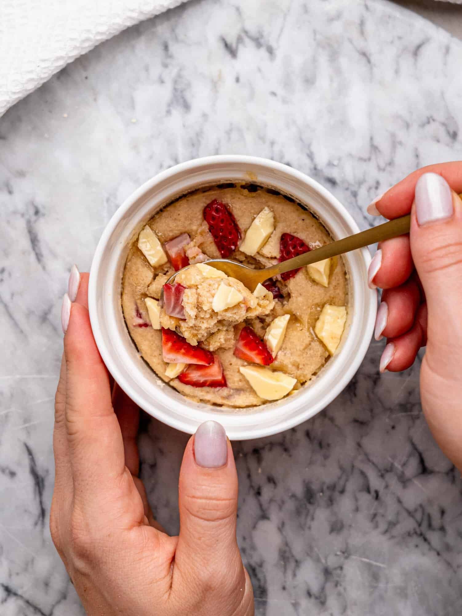 Strawberry white chocolate protein mug cake with a spoonful of the soft, cake-like center being lifted from the ramekin.
