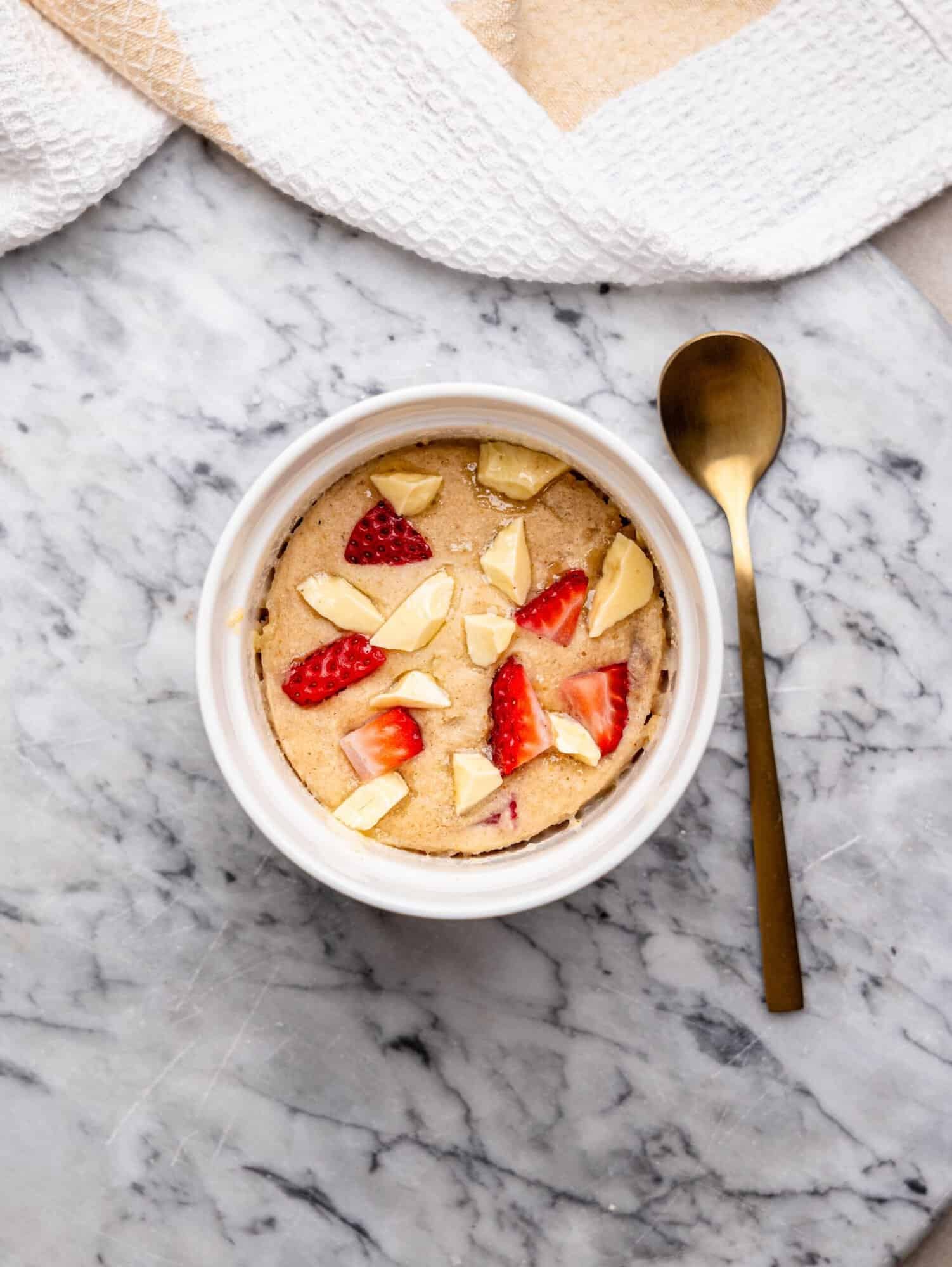 Strawberry white chocolate mug cake topped with fresh strawberries and white chocolate pieces, photographed from above.