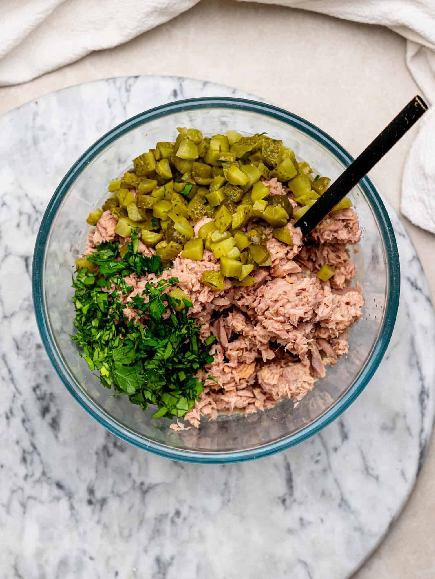 Canned tuna with chopped pickles and fresh parsley arranged in a mixing bowl before adding the creamy dressing.