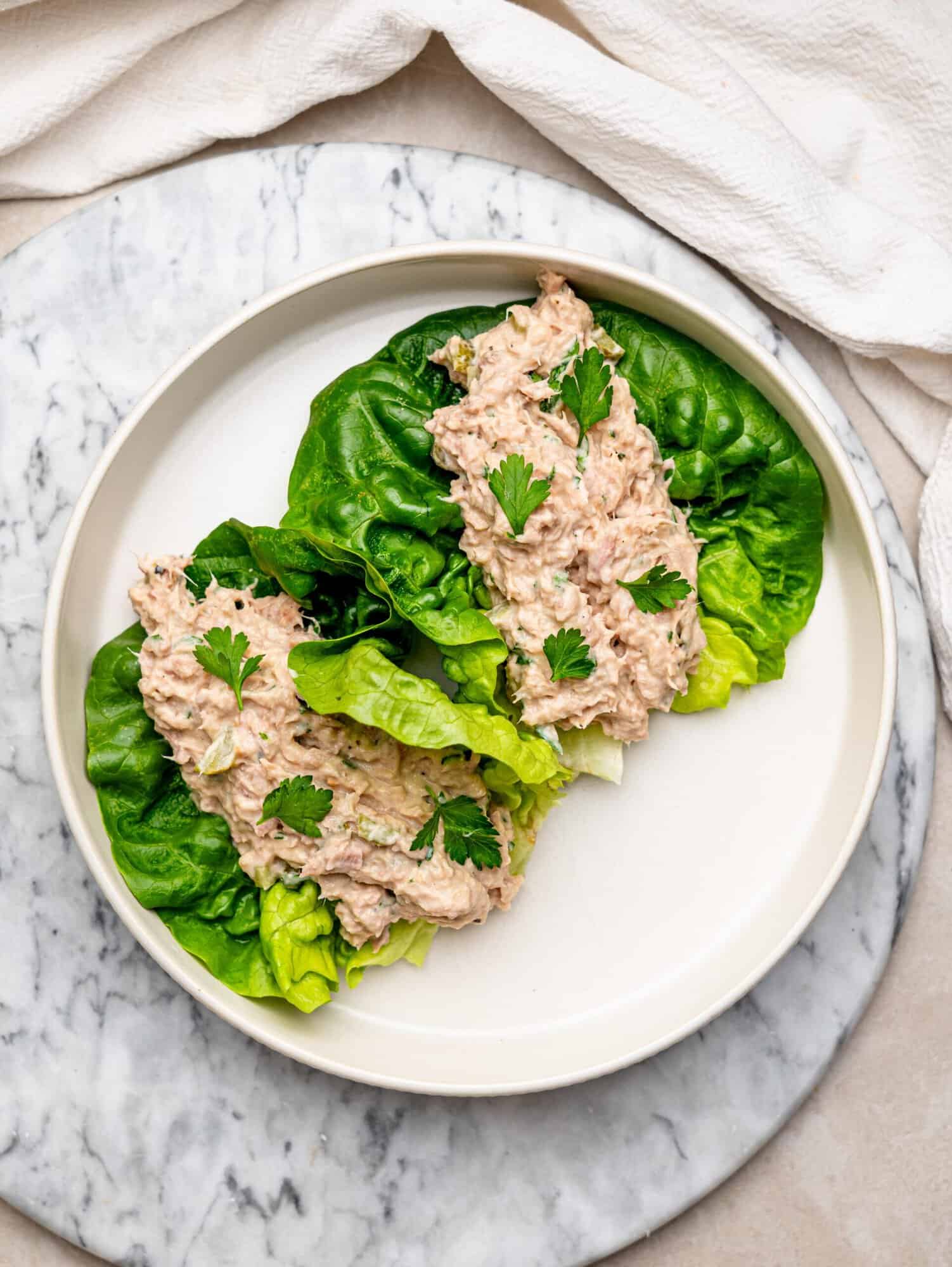 Creamy tuna salad served in fresh lettuce leaves and garnished with parsley on a white plate.